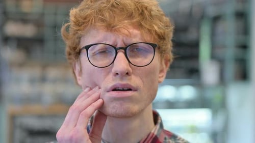Gros plan d'un jeune homme rousse ayant mal aux dents, carie