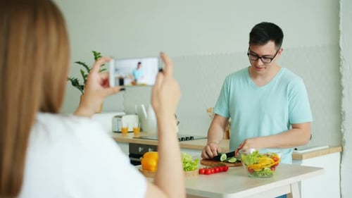 Couple of Vloggers Recording Video of Guy Cooking Salad in Kitchen at Home