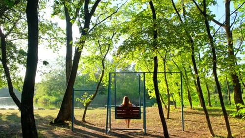 Femme se balançant sur balançoire. Fille solitaire en robe le soir d'été. Concept de rêves féminins.