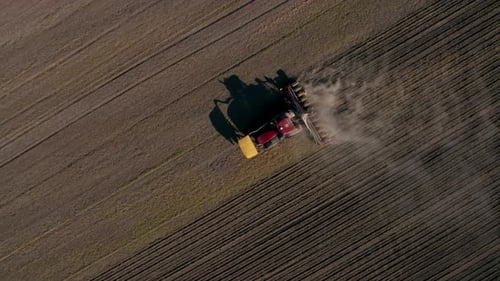 Aerial view of a moving tractor that plowing the fields