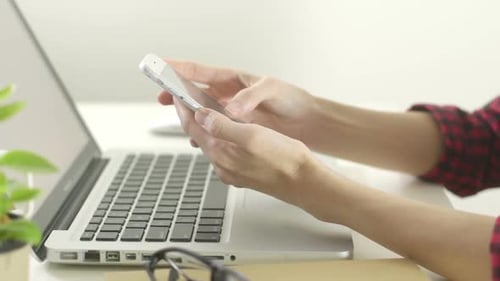 Hands Using Smartphone Next to Laptop Computer