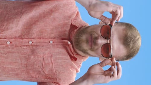 Man Putting on Sunglasses Against Blue Background
