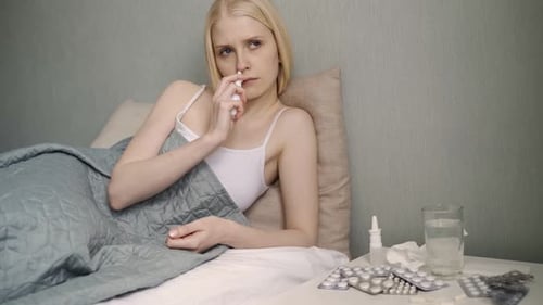 Woman Using Nasal Spray in Bed, Feeling Sick