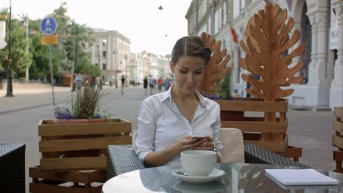 Young Woman Drinking Coffee and Using Her Mobile Phone in a Outdoor Cafe