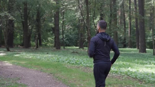 Adult Man Runs in the Park Camera Following Runner in Wireless Headphones Healthy Lifestyle in
