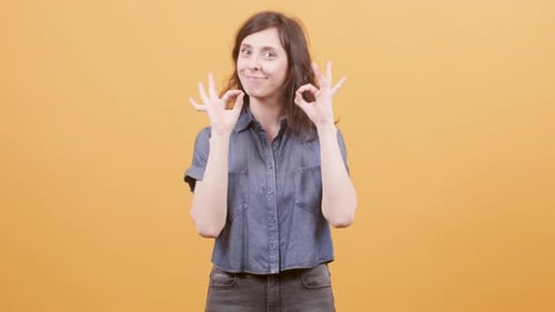 Smiling Woman Gives Ok Symbol on Orange Background