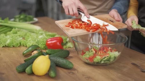 Nahaufnahme von Menschenhänden, die Gemüse auf einem Holzschneidebrett für Salat auf dem Tisch schneiden