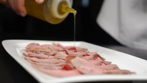 Chef Drizzling Sauce Over Thinly Sliced Roast Beef