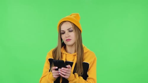 Portrait of Modern Girl in Yellow Hat Is Texting on Her Phone. Green Screen