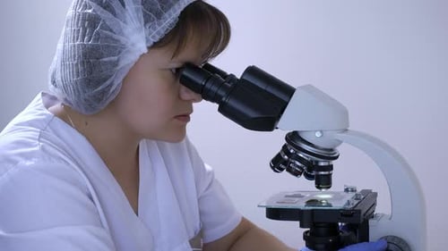 Woman Laboratory Technician Stares Into Eyepieces of a Microscope