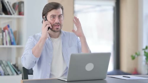 Frustrated Man Talking on Phone at Office Desk