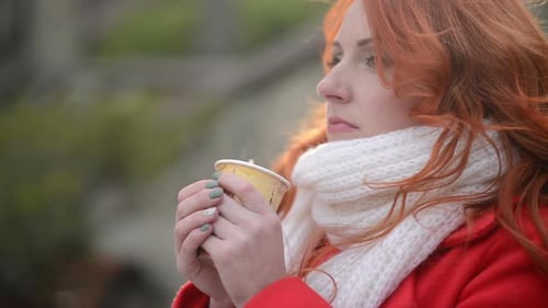 Woman with Red Hair Drinks Coffee Outdoors