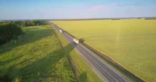 Highway with Driving Trucks Lorries Between Field and Groves