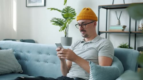 Man Using Smartphone on Blue Couch Indoors