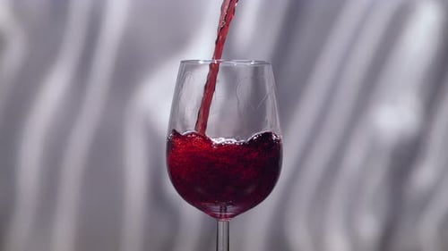 Red wine pouring in a glass on a grey background