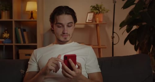 Crop View of Excited Young Man Scrolling Phone Screen and Saying Wow While Sitting on Sofa at Home