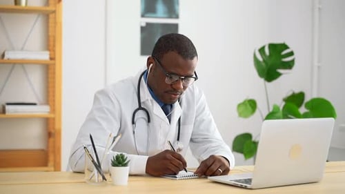 Young Male Doctor is Writing During Online Consultation at Table in Modern Clinic Spbas
