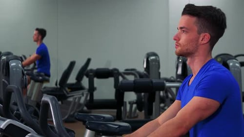 Ein junger fitter Mann trainiert auf einem Heimtrainer in einem Fitnessstudio - Nahaufnahme von der Seite