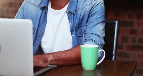 Mann trinkt Kaffee, während er am Laptop arbeitet