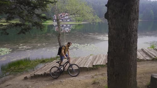 Man Walks Bike by Calm Lake in Nature
