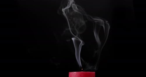 Red candle burning on black background. Blow out the candle. Smoke goes up. Close-up
