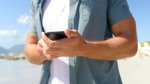 Mid section of man using mobile phone at beach on a sunny day 4k