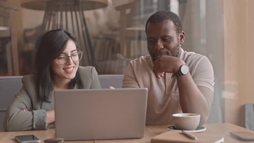 Diverse Business Couple Discussing Project on Laptop in Cafe
