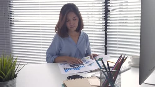 young smiling asian woman working on laptop while sitting in a living room at home.