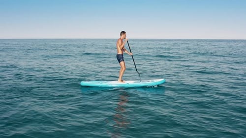 Man Paddleboarding on Turquoise Ocean, Aerial View