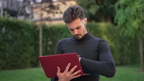 Busy Concentrated Caucasian Man Messaging Online on Laptop Standing in City Outdoors