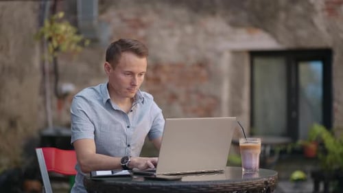 Freelancer Businessman in Glasses Diligently Working on Laptop in Cafe