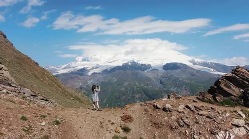 Woman Stands on Mountain Top and Takes Photos of Elbrus