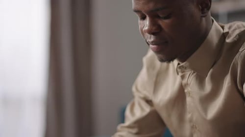 Afroamerican Guy is Surfing Internet By Smartphone Sitting in Living Room in Flat Viewing Photos in