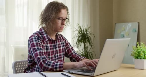 A young man works on a computer while sitting in the interior. A student uses a laptop for online
