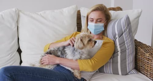 Woman wearing face mask holding her pet dog at home