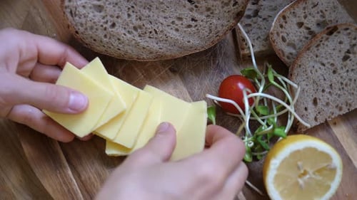 Top View of Hands Putting Slices of Vegan Cheese Next To Rye Bread and Vegetables on Wooden Board