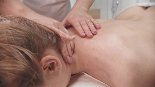 Ruhende Frau liegt auf der Couch im Kabinett der Masseuse, während sie sanft ihren Hals massiert