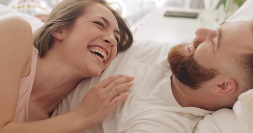 Nahaufnahme eines glücklichen Paares, das am frühen Morgen auf dem Bett liegt, redet und lacht. Schöne Frau