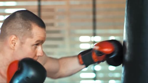 Young Boxer is Exercising with a Punching Bag at the Gym