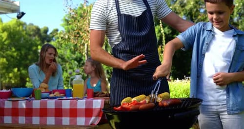 Father and son grilling sausages and corns on barbecue