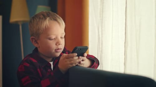 Blond Boy Using Smartphone Leaning on Sofa