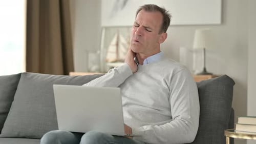 Man Rubbing Stiff Neck While Using Laptop
