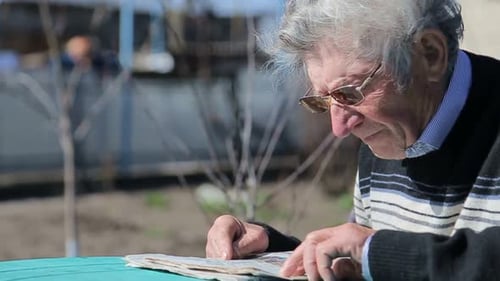 Senior Man Reading Newspaper at Outdoor Table