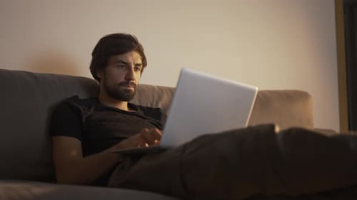 Man Using Laptop While Lying on Couch