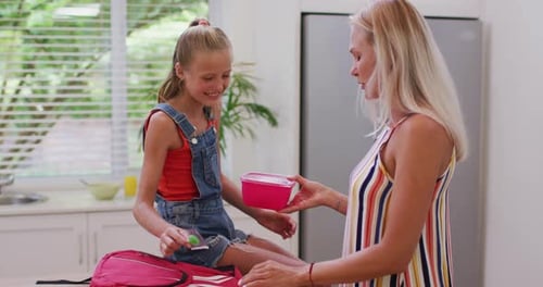 Girl Packing Lunch with Mother in Kitchen