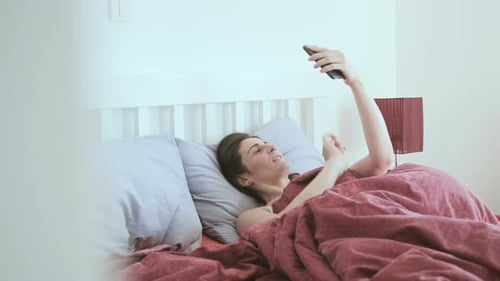 Woman Using Phone Lying in Bed Indoors