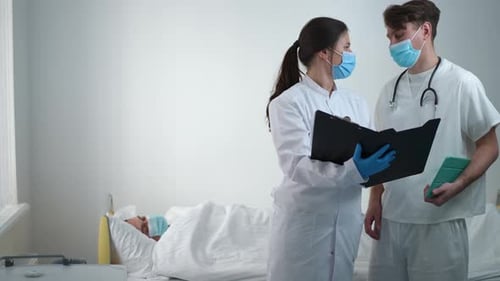 Besorgte männliche und weibliche Ärzte sprechen im Stehen in der Krankenstation rechts mit verschwommenem Patienten