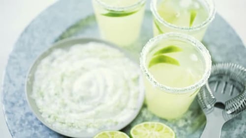 Key lime margarita garnished with fresh lime and salt in mason jar on metal tray.
