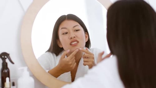 Young Woman Popping Pimple in Bathroom Mirror