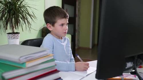 Boy Writing at Desk with Computer